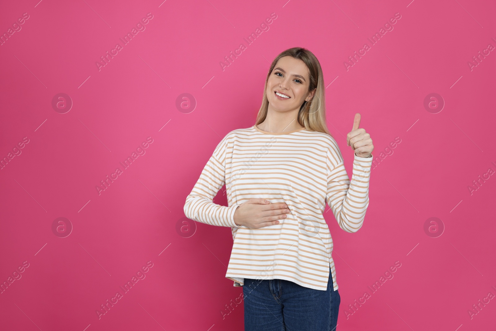 Photo of Happy woman touching her belly and showing thumb up on pink background, space for text. Concept of healthy stomach