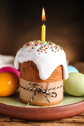 Photo of Traditional Easter cake with burning candle on wooden table against black background