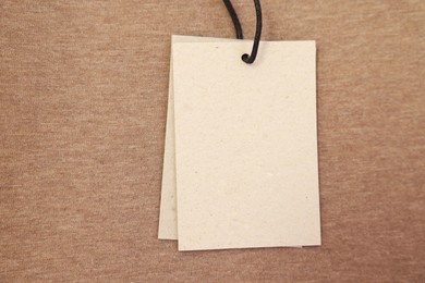 Photo of Cardboard tags on brown garment, top view. Space for text