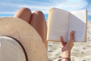 Photo of Woman reading book on sandy beach near sea, closeup