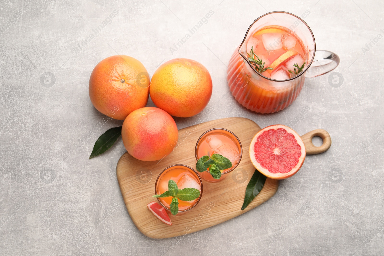 Photo of Tasty freshly made grapefruit juice, fruits and mint on light grey table, flat lay