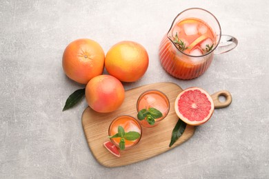 Photo of Tasty freshly made grapefruit juice, fruits and mint on light grey table, flat lay