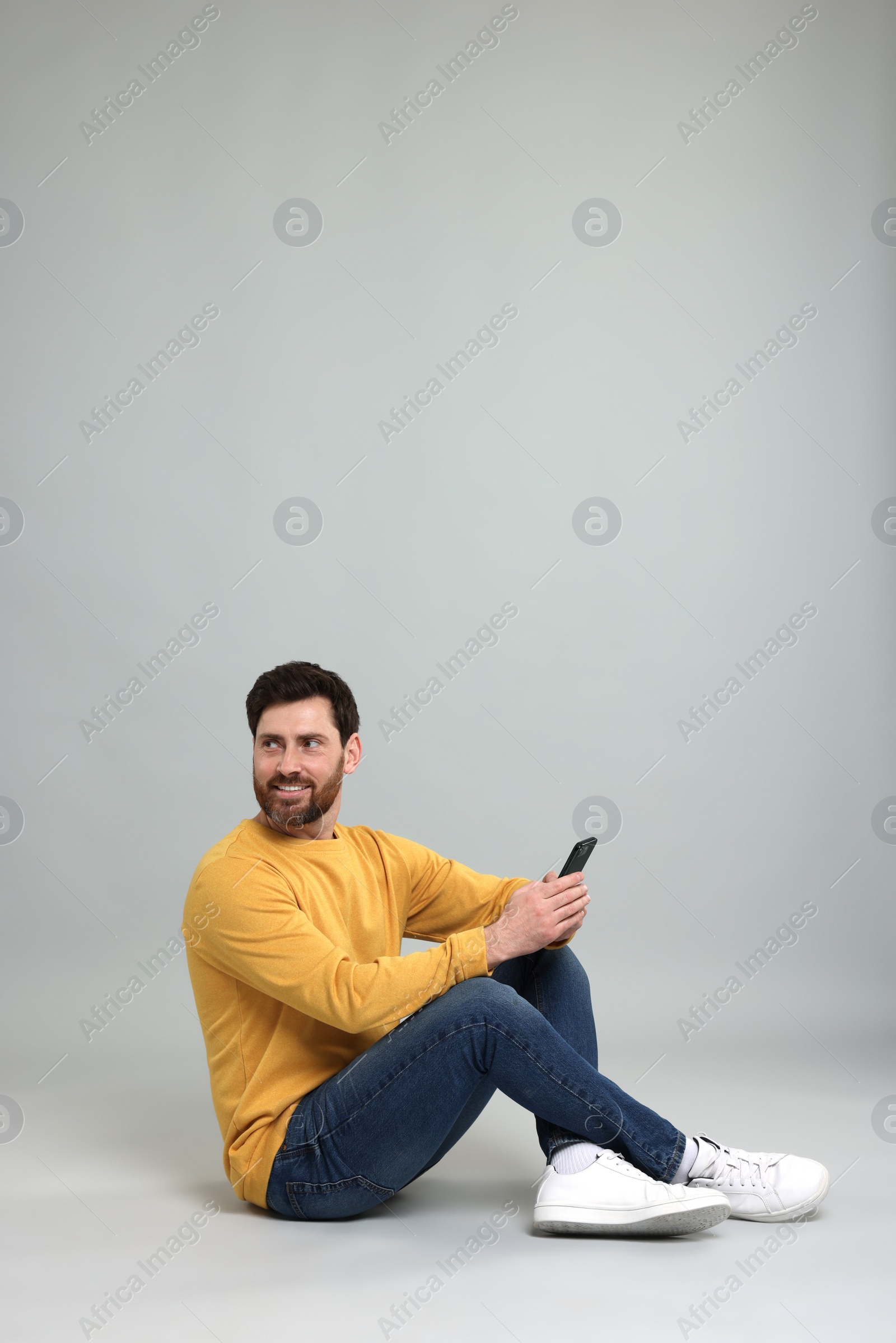 Photo of Smiling man with smartphone on grey background. Space for text