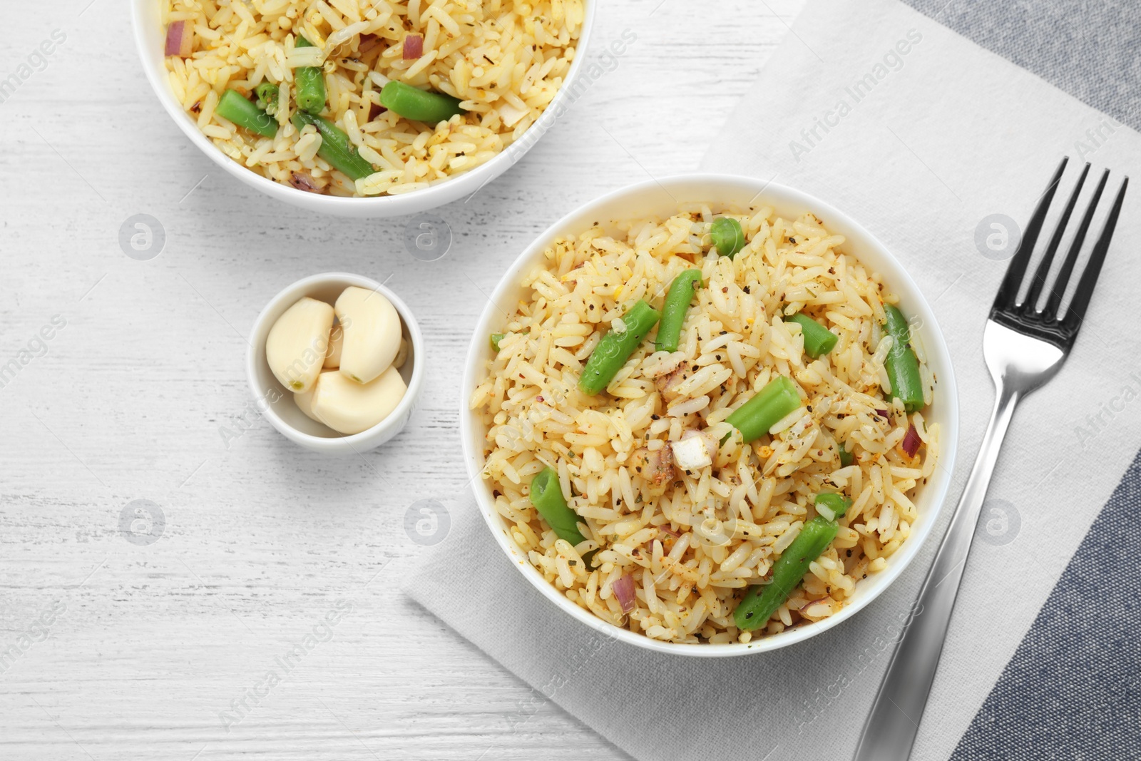 Photo of Tasty rice pilaf with vegetables served on white wooden table, flat lay