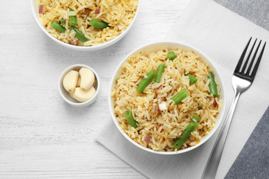 Photo of Tasty rice pilaf with vegetables served on white wooden table, flat lay