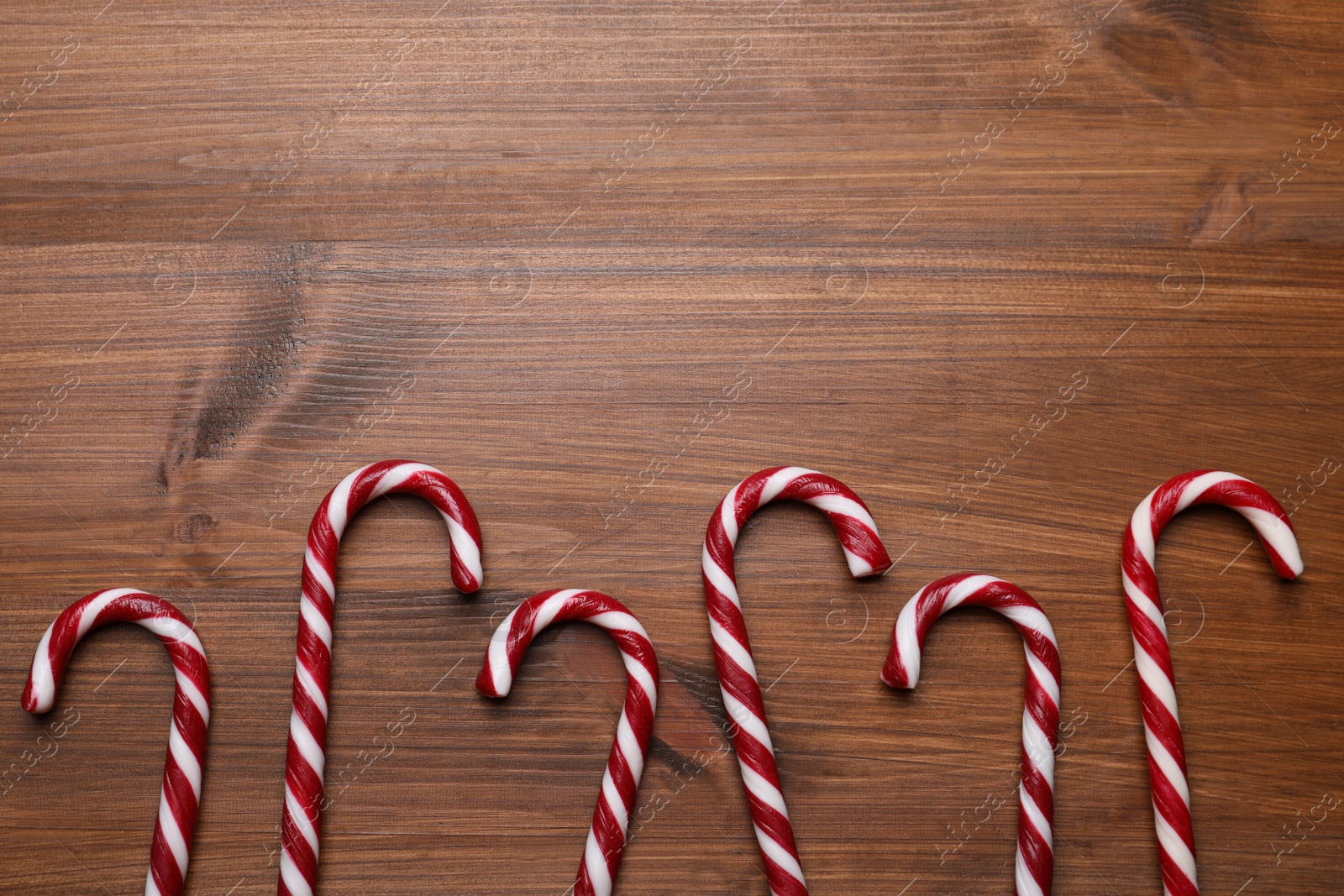 Photo of Sweet Christmas candy canes on wooden table, flat lay. Space for text