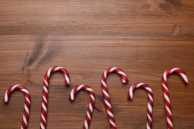 Sweet Christmas candy canes on wooden table, flat lay. Space for text