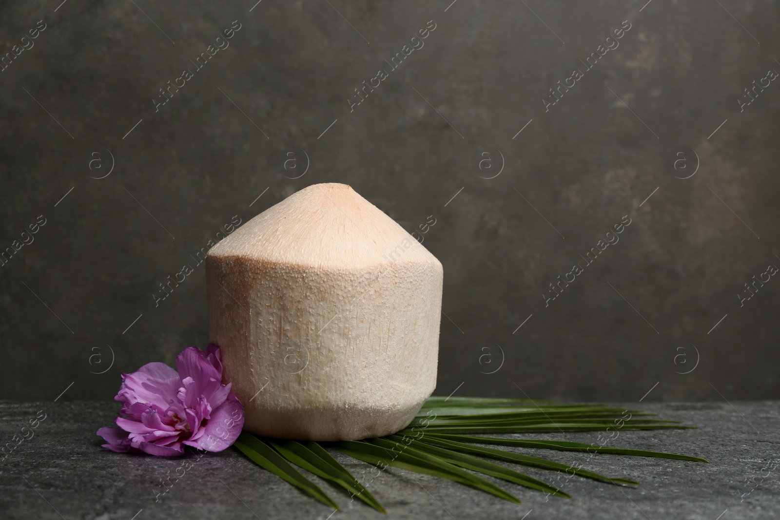 Photo of Young peeled coconut with palm leaf and flower on grey table