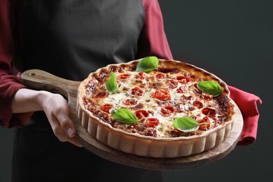 Photo of Woman holding delicious homemade quiche with prosciutto on dark background, closeup