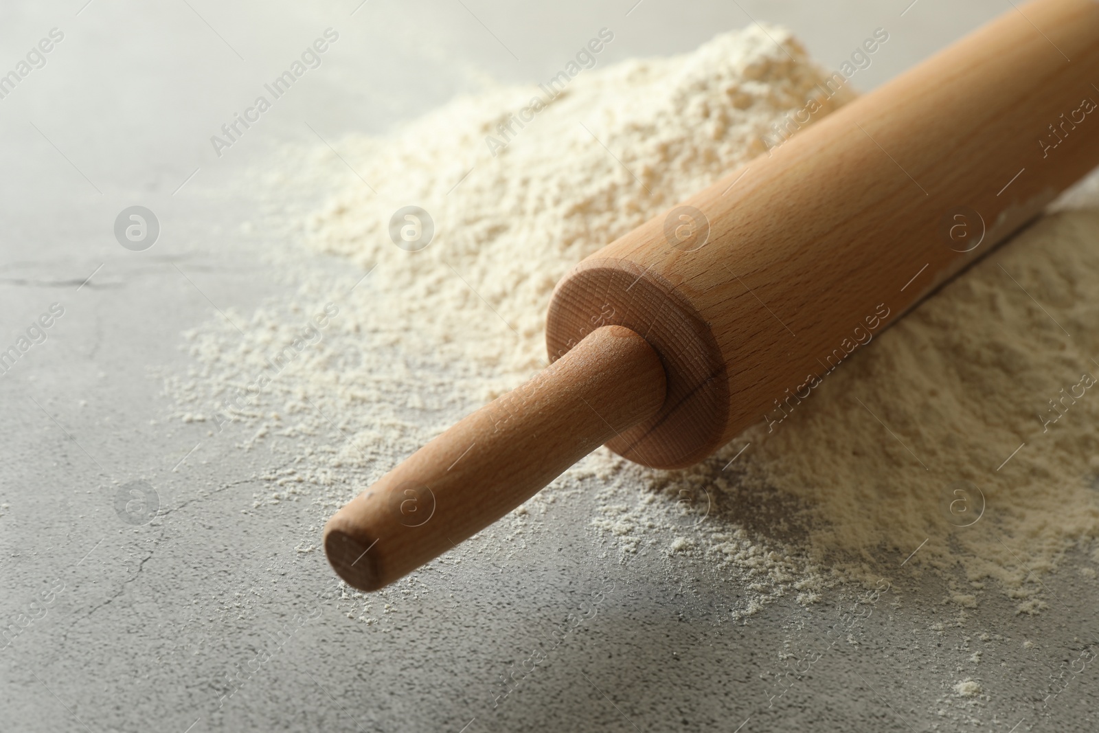 Photo of Flour and rolling pin on grey table, closeup. Space for text
