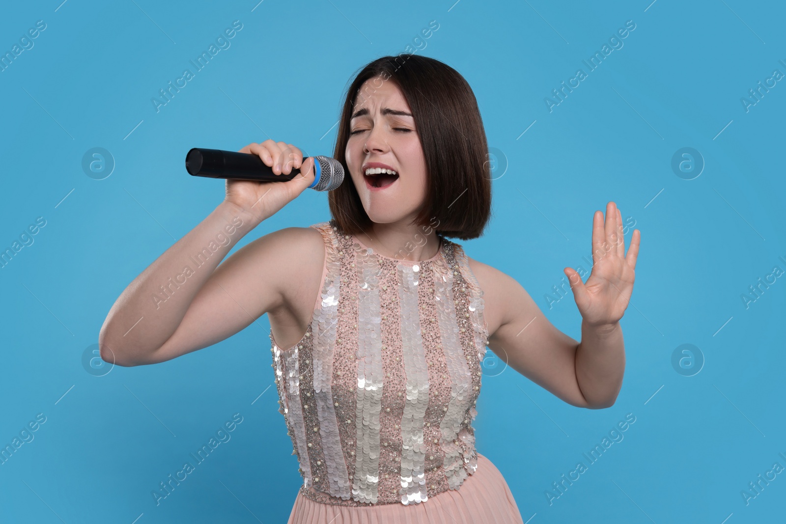 Photo of Beautiful young woman with microphone singing on light blue background