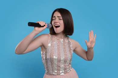 Beautiful young woman with microphone singing on light blue background