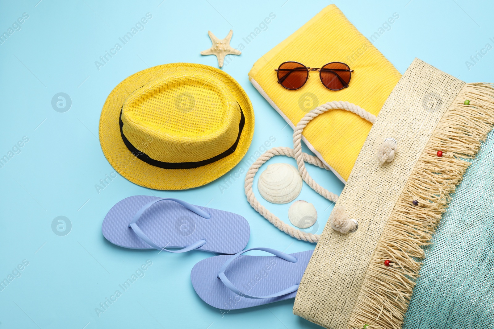 Photo of Stylish bag with beach accessories on turquoise background, flat lay