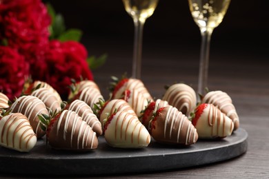 Photo of Delicious chocolate covered strawberries, sparkling wine and flowers on wooden table