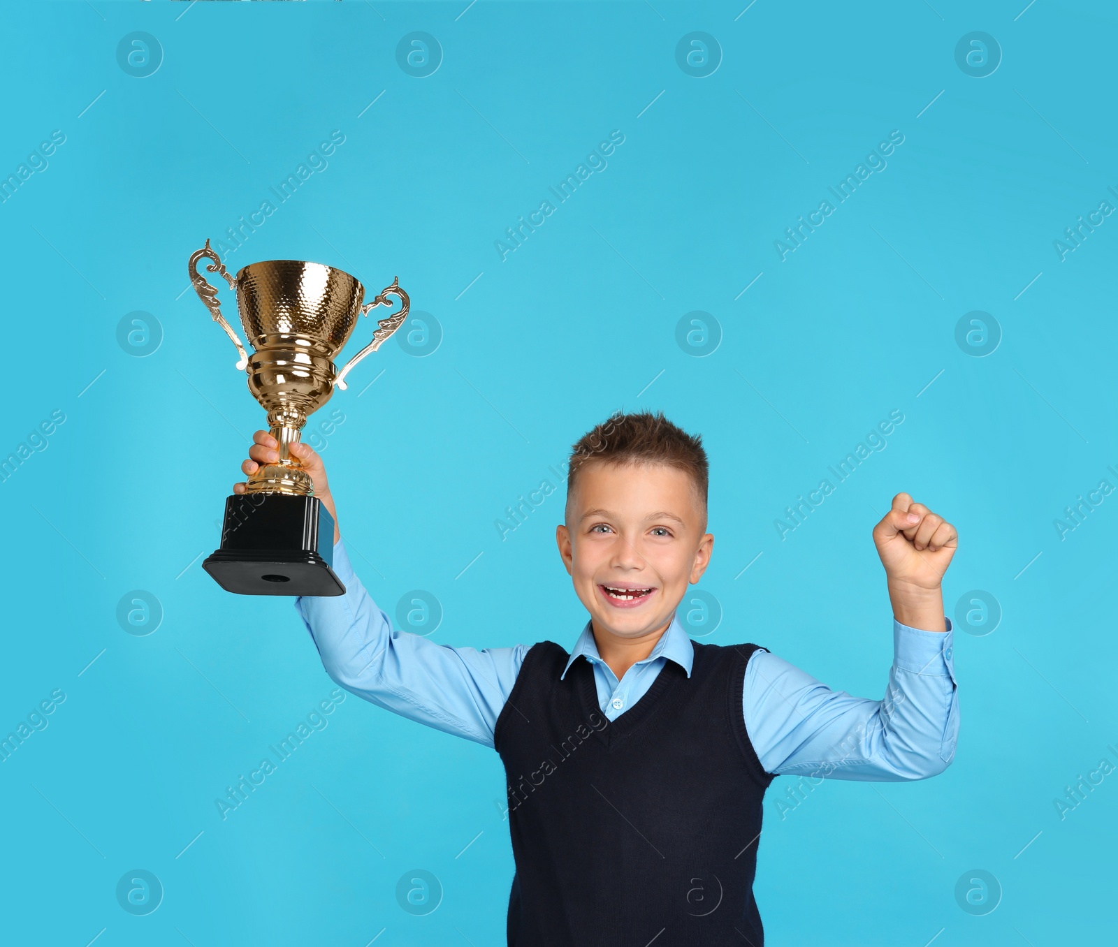 Photo of Happy boy in school uniform with golden winning cup on blue background