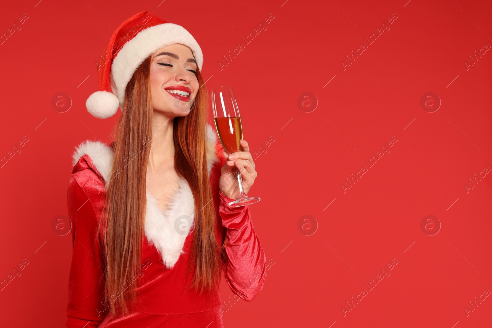 Photo of Young woman in Santa hat with glass of wine on red background, space for text. Christmas celebration