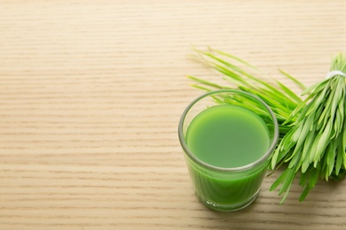 Photo of Shot glass of wheat grass juice and sprouts on wooden table, space for text