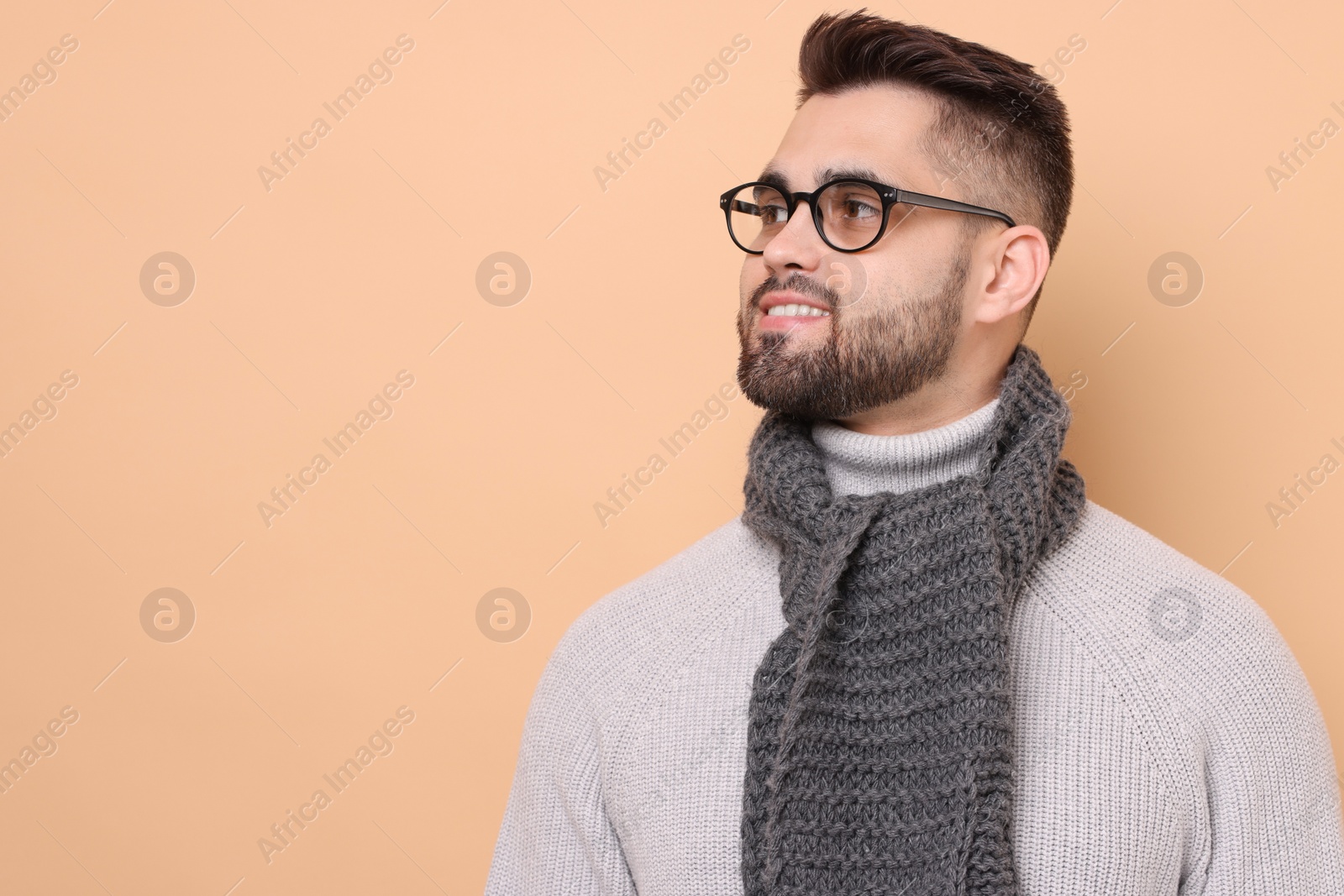 Photo of Smiling man in knitted scarf on beige background. Space for text