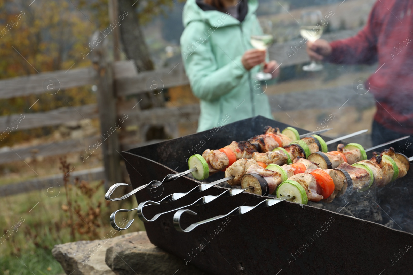 Photo of Couple having barbecue party outdoors, focus on brazier with meat and vegetables