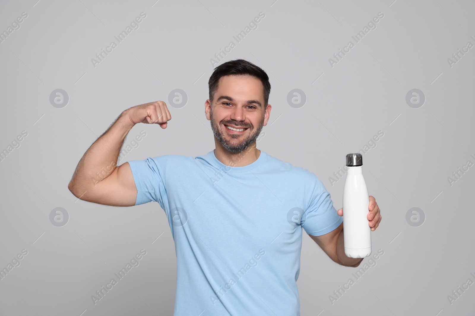 Photo of Happy man holding thermo bottle and showing arm on light grey background