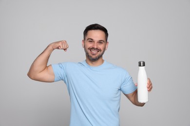 Photo of Happy man holding thermo bottle and showing arm on light grey background