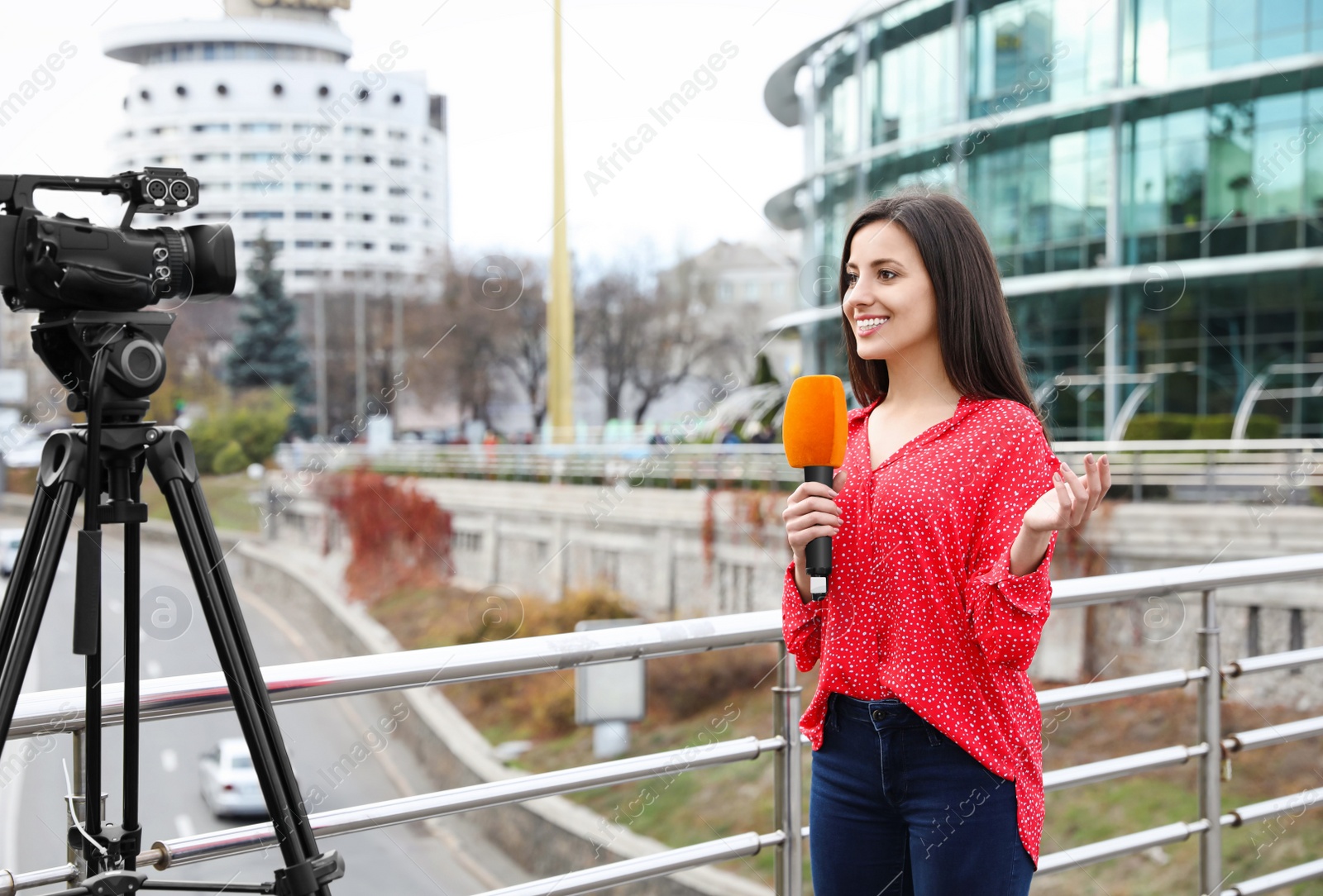 Photo of Young female journalist with microphone working on city street