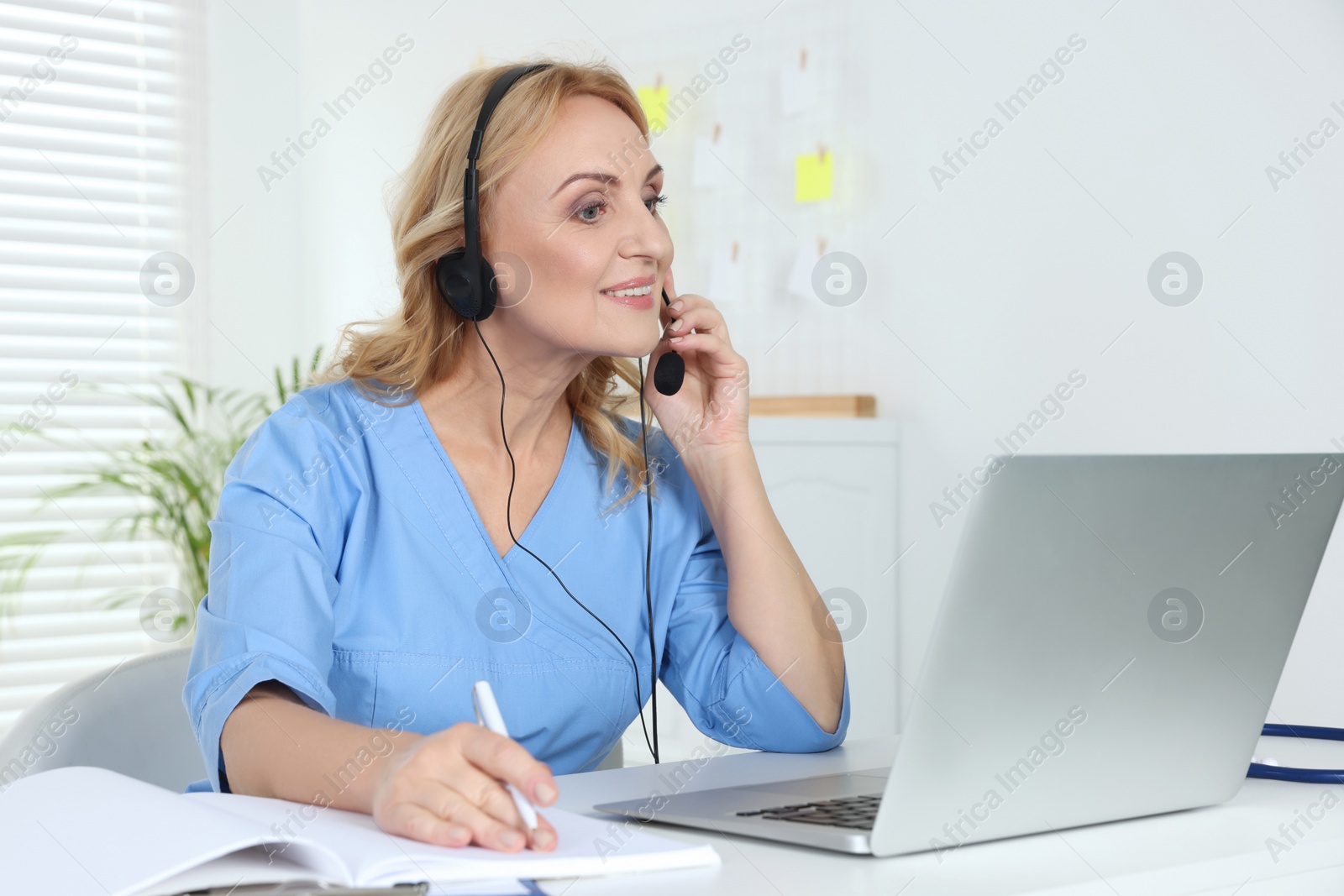 Photo of Doctor with laptop and headphones consulting patient in clinic. Online medicine concept