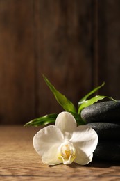 Spa stones, beautiful orchid flower and bamboo sprout on wooden table, closeup. Space for text