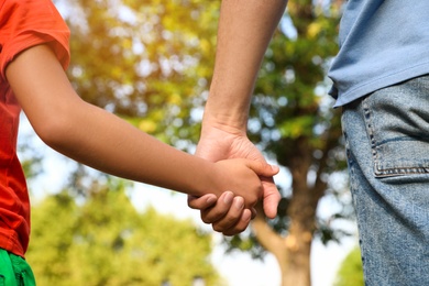 Photo of Little boy and his father holding hands outdoors, closeup. Family weekend