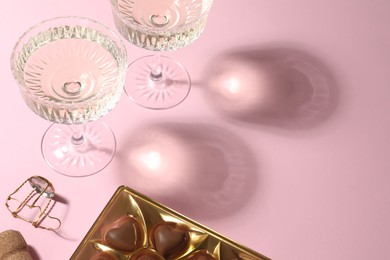 Photo of Glasses of expensive white wine, cork and heart shaped chocolate candies on pink background. Space for text