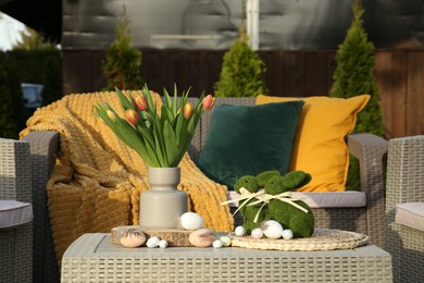 Terrace with Easter decorations. Bouquet of tulips in vase, bunny figures and decorative eggs on table outdoors