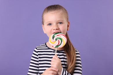 Photo of Cute little girl licking colorful lollipop swirl on violet background