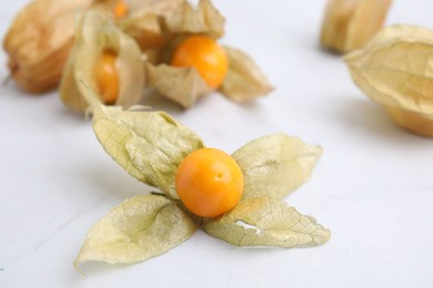 Ripe physalis fruits with calyxes on white marble table, closeup