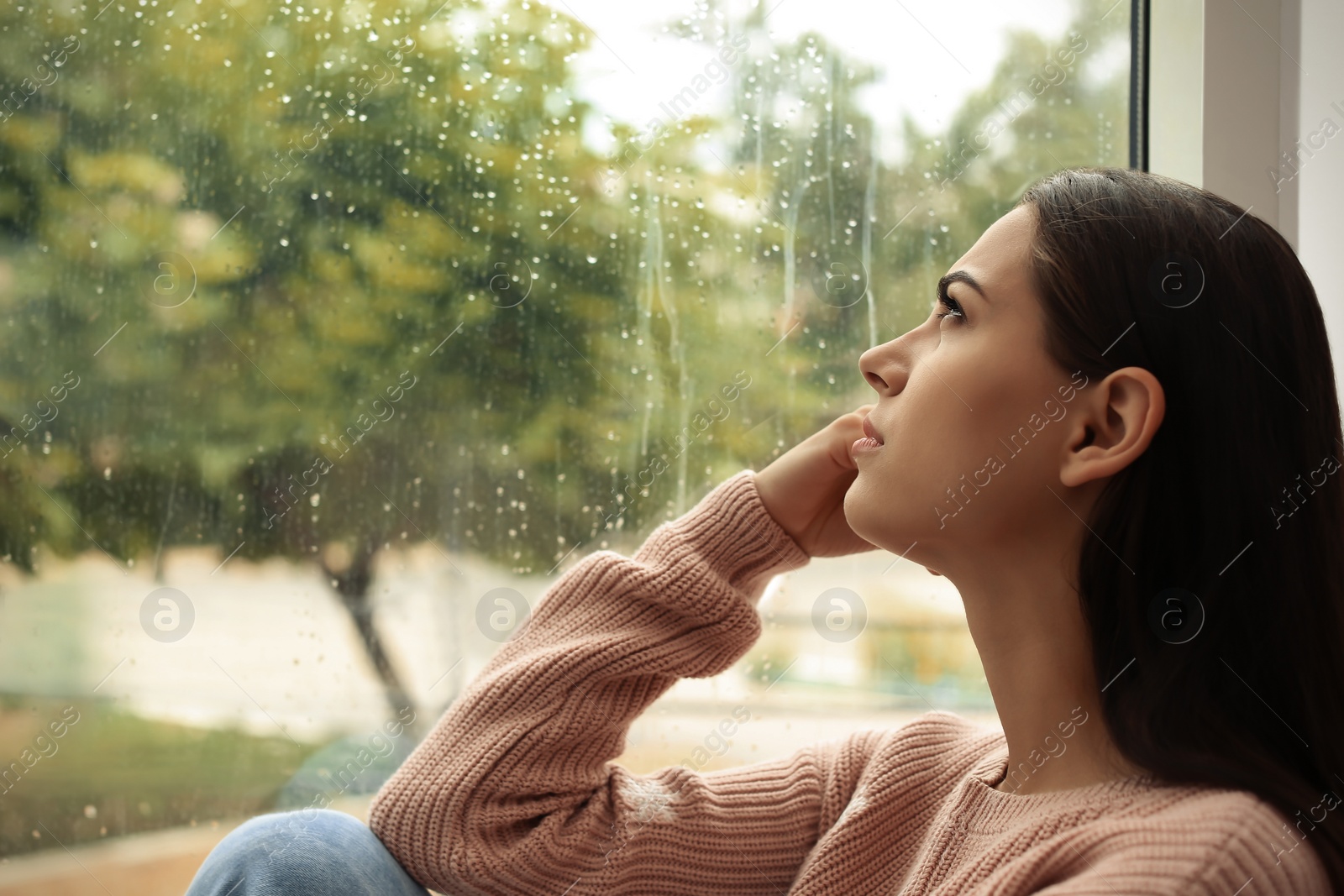 Photo of Young sad woman sitting near window at home