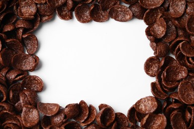 Photo of Breakfast cereal. Frame made of chocolate corn flakes on white background, top view. Space for text