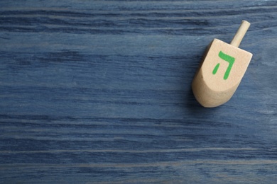 Photo of Hanukkah traditional dreidel with letter He on blue wooden table, top view. Space for text