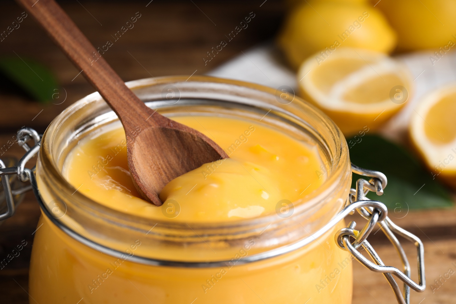 Photo of Wooden spoon in jar with lemon curd on table, closeup