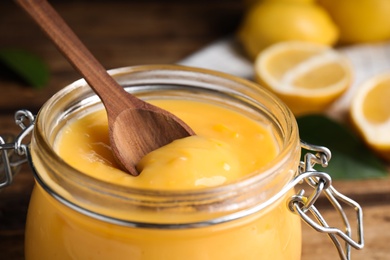 Photo of Wooden spoon in jar with lemon curd on table, closeup