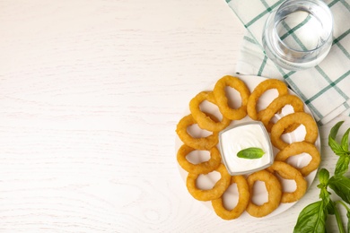 Delicious onion rings with sauce on white wooden table, flat lay. Space for text