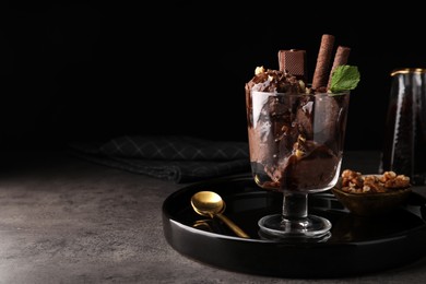 Tasty chocolate ice cream with sauce, nuts and wafer rolls in glass dessert bowl on dark grey table. Space for text