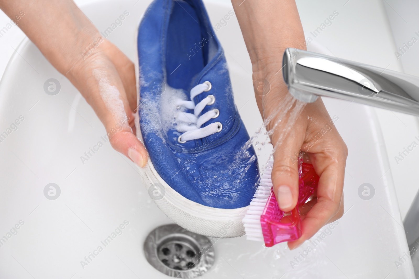 Photo of Woman washing shoe with brush under tap water in sink, closeup