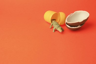 Photo of Slynchev Bryag, Bulgaria - May 25, 2023: Halves of Kinder Surprise Egg, plastic capsule and toy crocodile on orange background, space for text