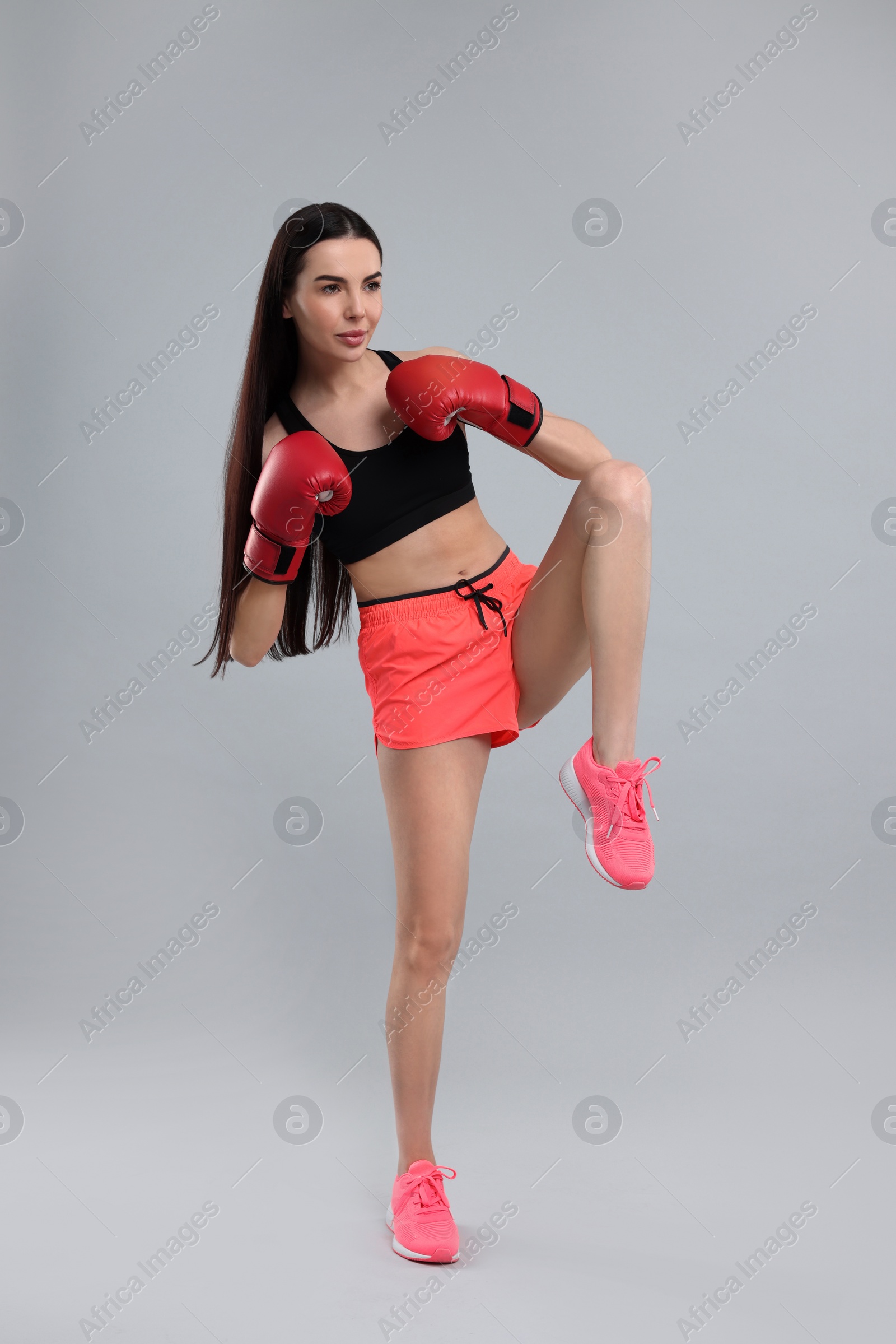 Photo of Beautiful woman in boxing gloves training on grey background