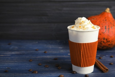 Takeaway paper cup with pumpkin spice latte and whipped cream on wooden table. Space for text