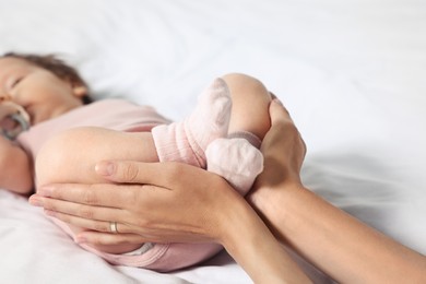 Mother holding legs of her little baby on bed, closeup