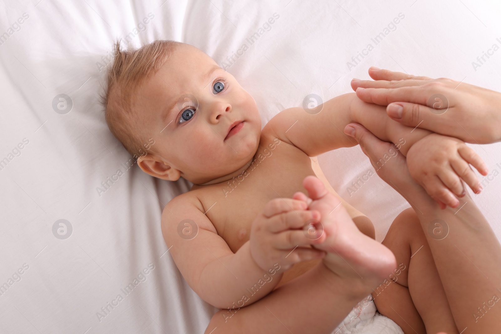 Photo of Mother massaging her cute baby with oil on bed, closeup