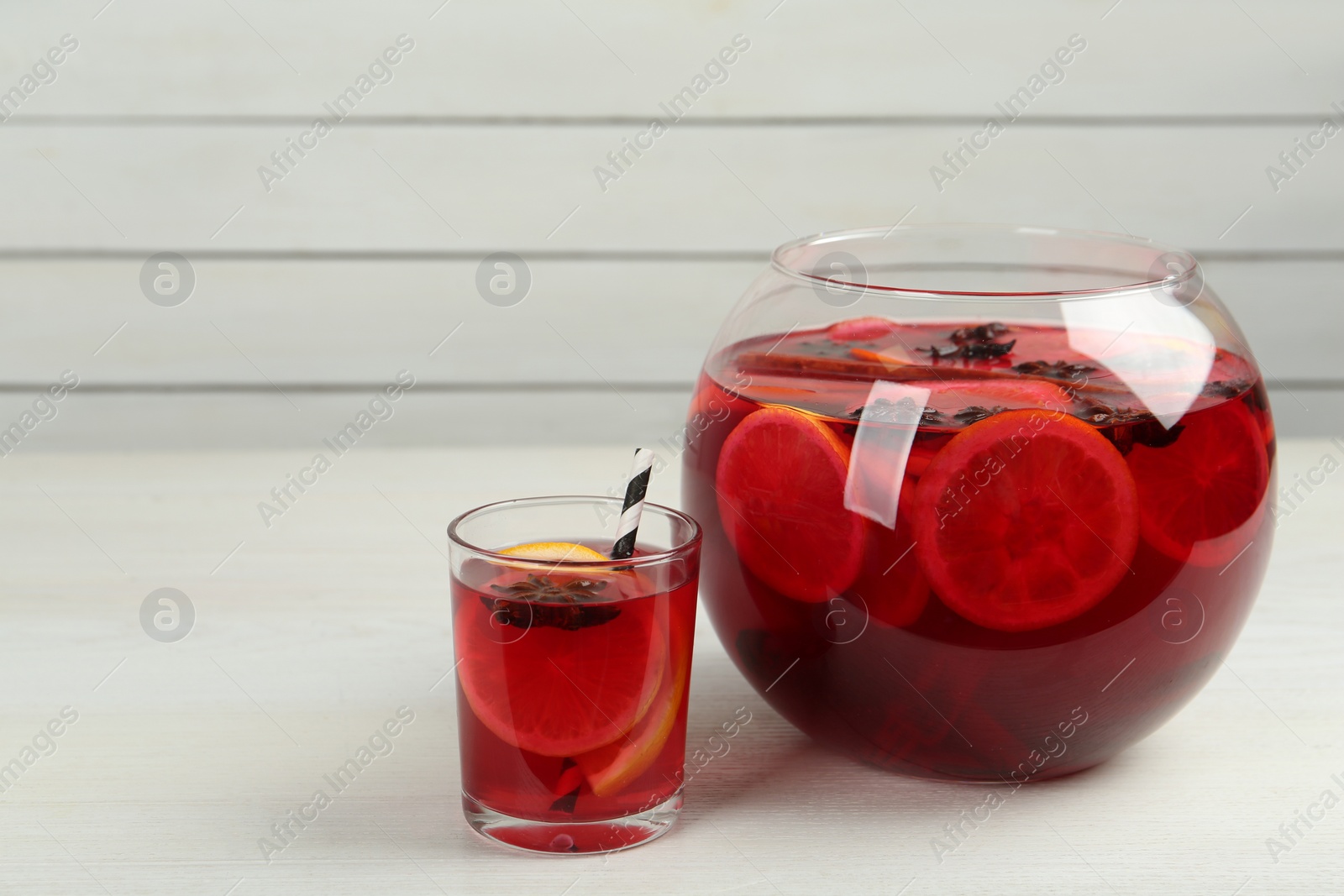 Photo of Glass and bowl of delicious aromatic punch drink on white wooden table. Space for text