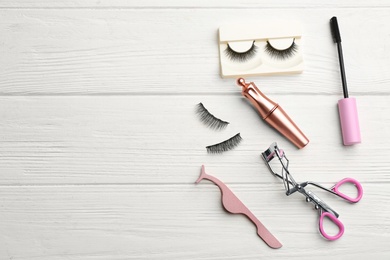 Flat lay composition with magnetic eyelashes and accessories on white wooden table. Space for text