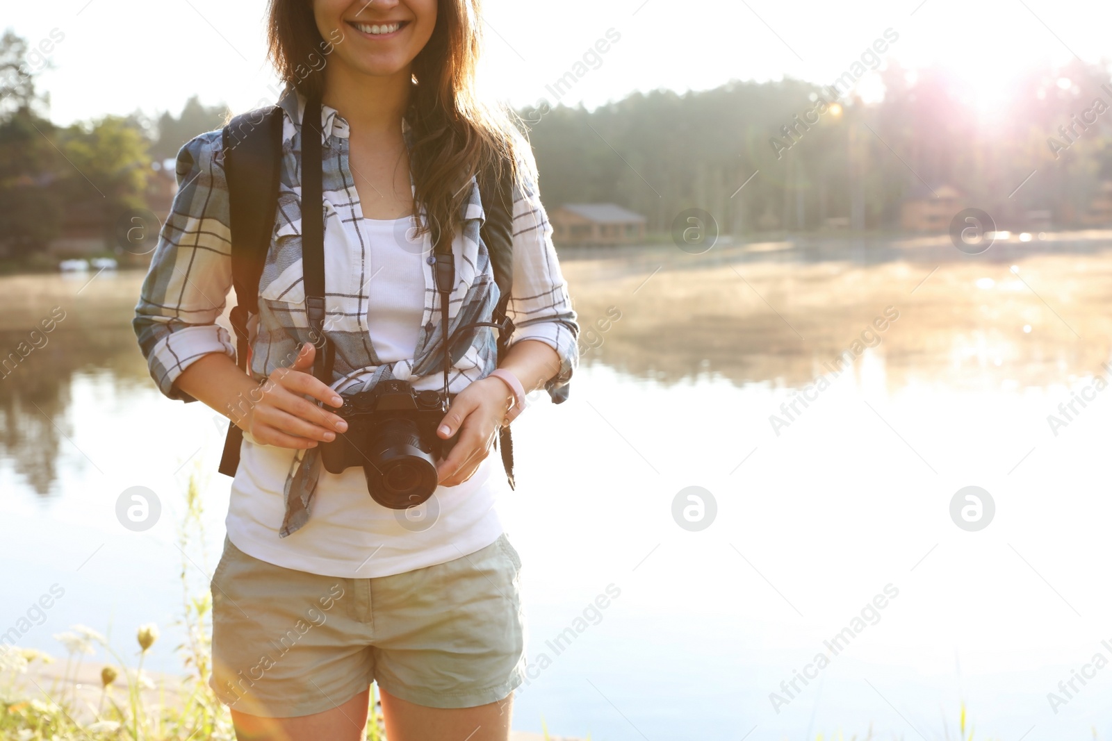 Photo of Young female photographer with camera near lake. Camping season
