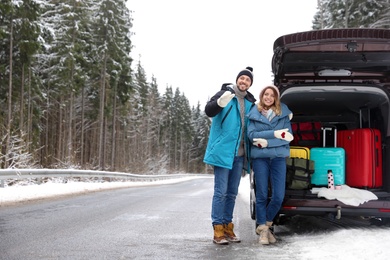 Couple near open car trunk full of luggage on road, space for text. Winter vacation